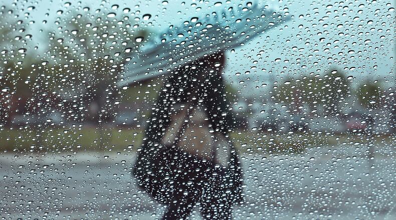 A man walks past a rain soaked window along High Street in Springfield with an umbrella during a downpour. BILL LACKEY/STAFF