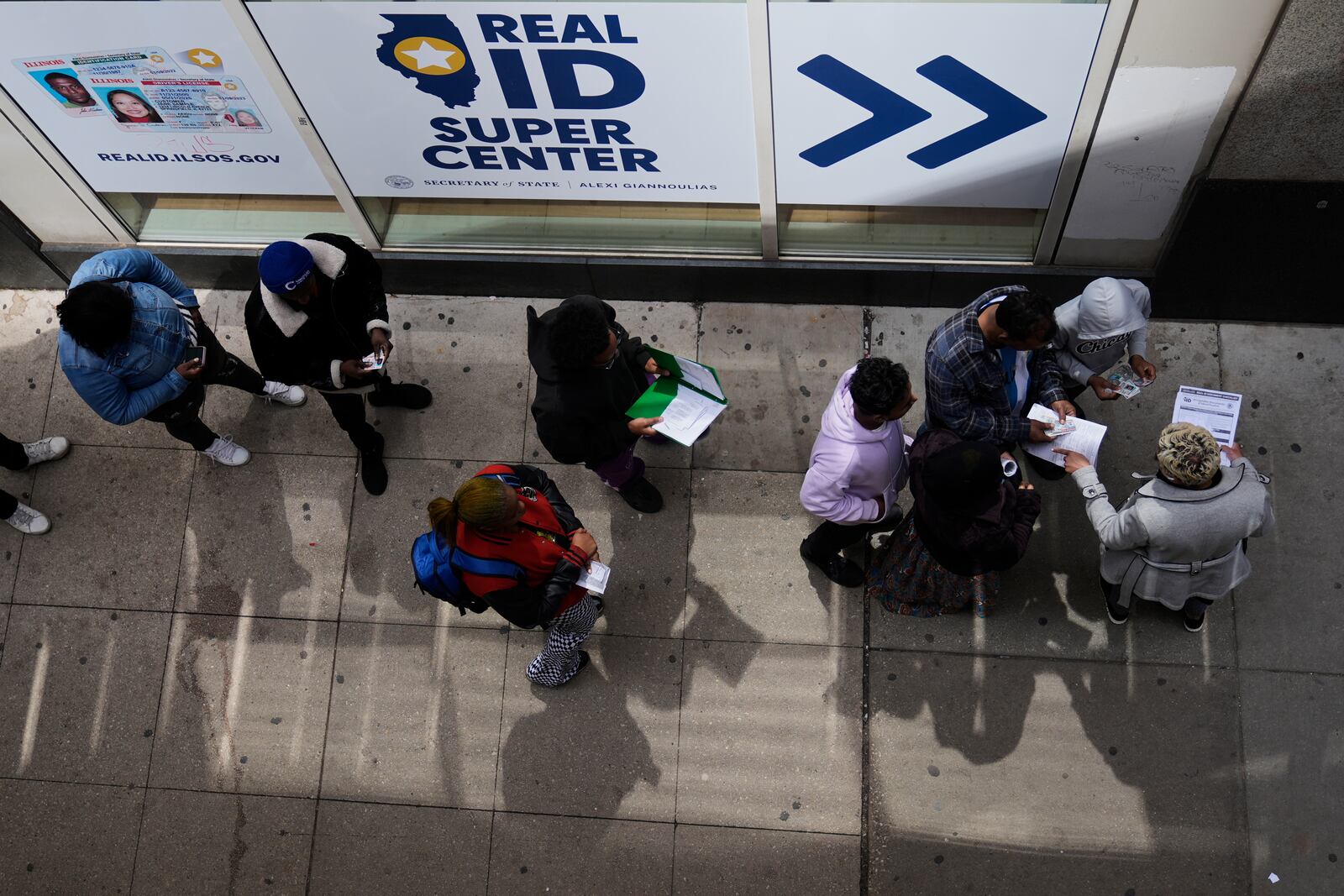 An employee, right, checks on necessary documents as people line up to apply for Real ID at a Real ID Supercenter in downtown Chicago, Tuesday, May 6, 2025. (AP Photo/Kiichiro Sato)