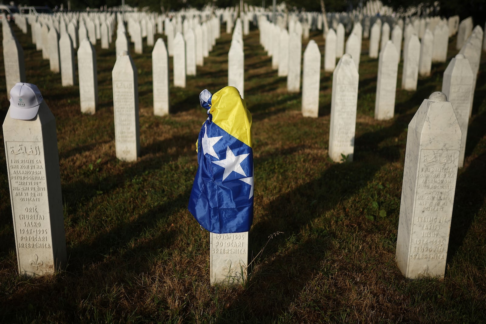 A Bosnian flag is seen at a grave stone at the Memorial Center for those killed in Srebrenica genocide in Potocari, Bosnia, Friday, July 11, 2025. (AP Photo/Armin Durgut)