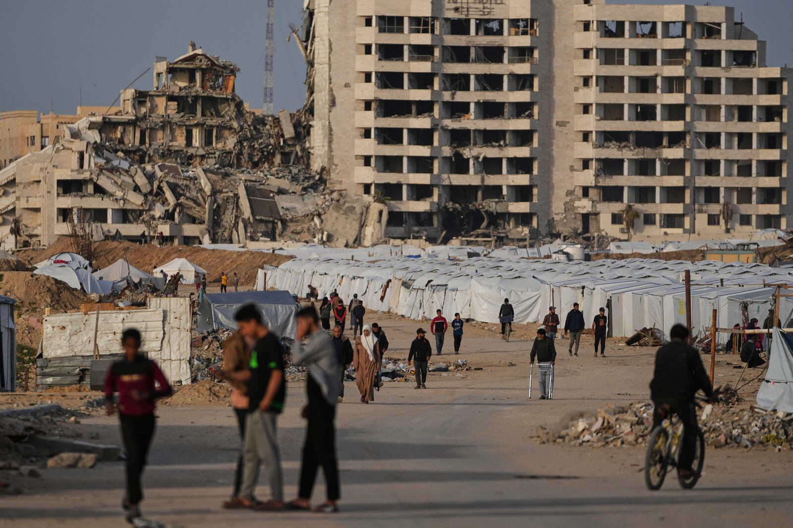 Palestinians walk next to a tent camp for displaced by the Israeli air and ground offensive on the Gaza Strip in west of Gaza Strip, Tuesday, March 25, 2025. (AP Photo/Jehad Alshrafi)