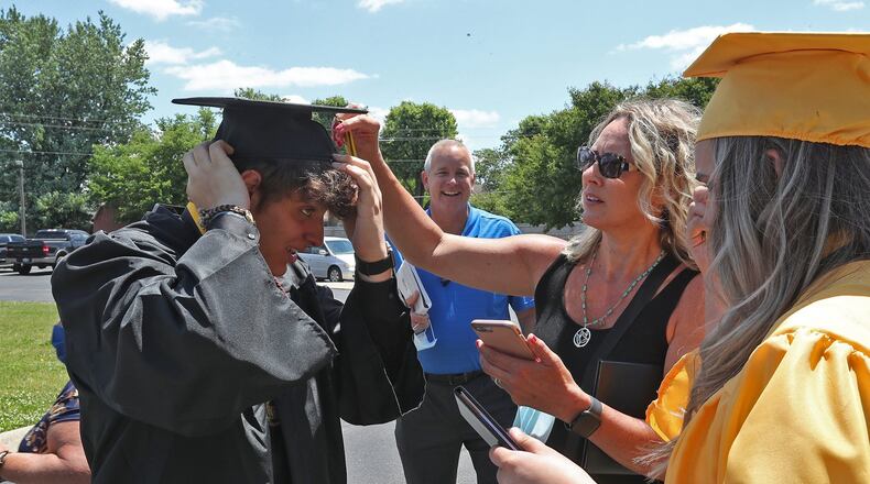 Shawnee graduate Matt Kendall gets some help putting on his cap from fellow graduate Isabelle Lee and her family in the parking lot of Southgate Baptist Church. BILL LACKEY/STAFF