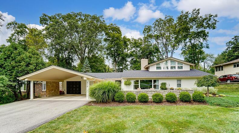 The front of the mid-century modern tri level has a stone accent wall, attached carport and one car attached garage and picture window