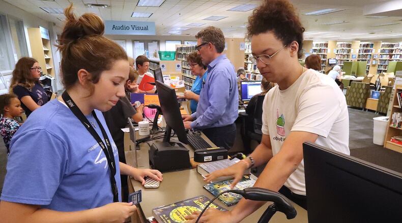 Levi Logan checks out some books for Sarah Beattie Tuesday at the Champaign County Library in Urbana. The library is temporarily suspending late fees. BILL LACKEY/STAFF