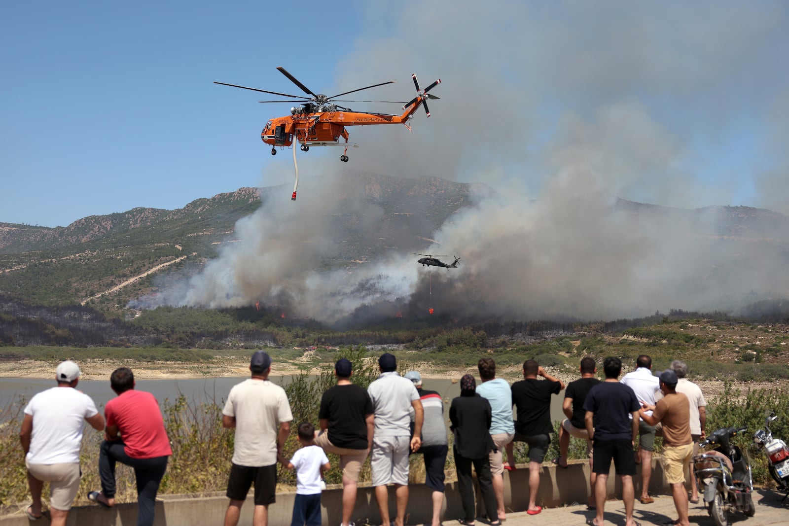 Helicopters spray water to extinguish a fire in Seferihisar, near Izmir, Turkey, Monday, June 30, 2025. (Cengiz Malgir/Dia Photo via AP)