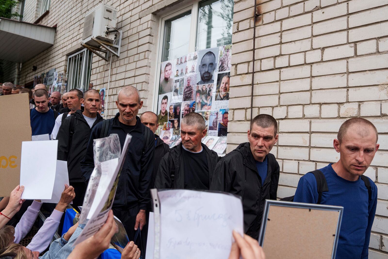 Ukrainian soldiers walk though human corridor with people holding photos of their missed relatives after returning from captivity after a POWs exchange between Russia and Ukraine, in Chernyhiv region, Ukraine, Saturday, May 24, 2025. (AP Photo/Evgeniy Maloletka)