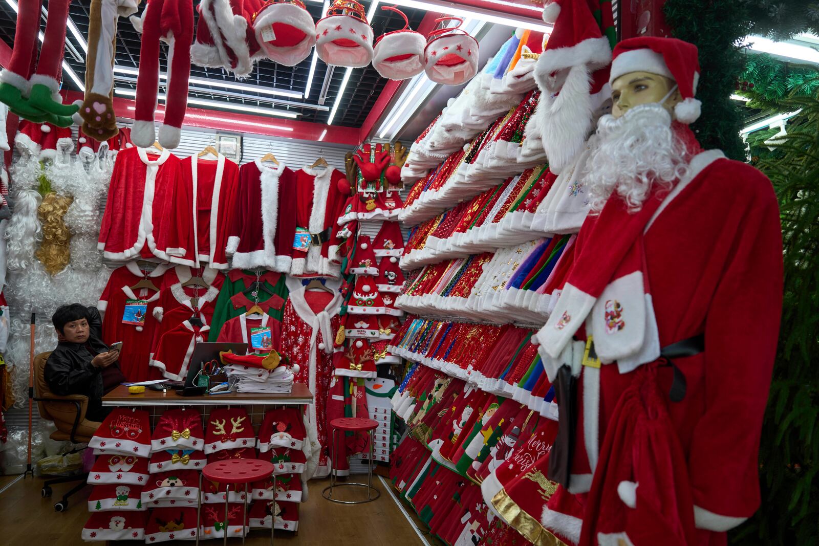 A vendor waits for customers near Santa costumes for sale at the Yiwu International Trade Market in Yiwu, eastern China's Zhejiang province on Thursday, April 10, 2025. (AP Photo/Ng Han Guan)