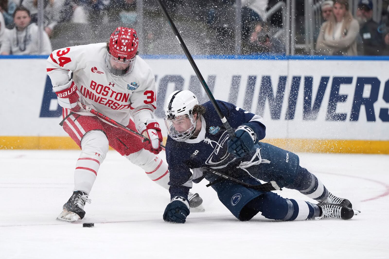 Penn State's Casey Aman, right, falls after colliding with Boston University's Cole Eiserman (34) during the third period in a semifinal game in the NCAA Frozen Four men's college hockey tournament, Thursday, April 10, 2025, in St. Louis (AP Photo/Jeff Roberson)