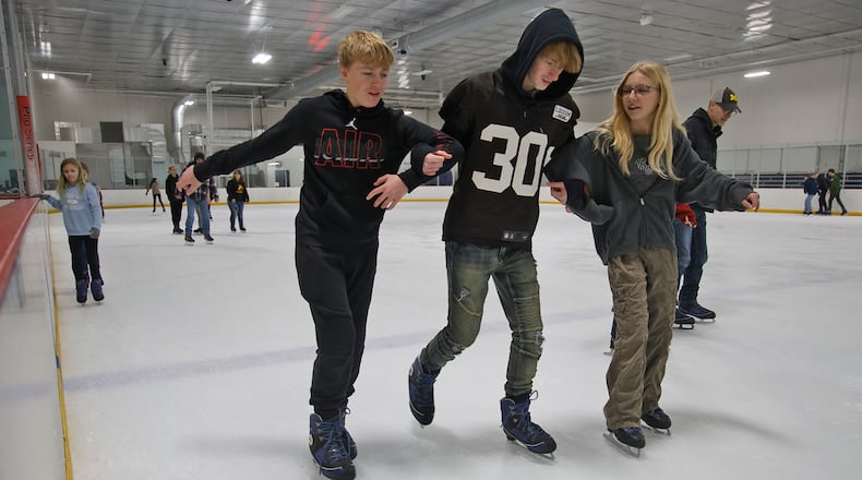 Three friends, from left, Tarrence Chapman, Christian Cloud and Kyndall Brown link arms for stability as they work their way aroung the ice Friday, Dec. 29, 2023 at National Trail Parks and Recreation District's Chiller Ice Skating Rink. BILL LACKEY/STAFF