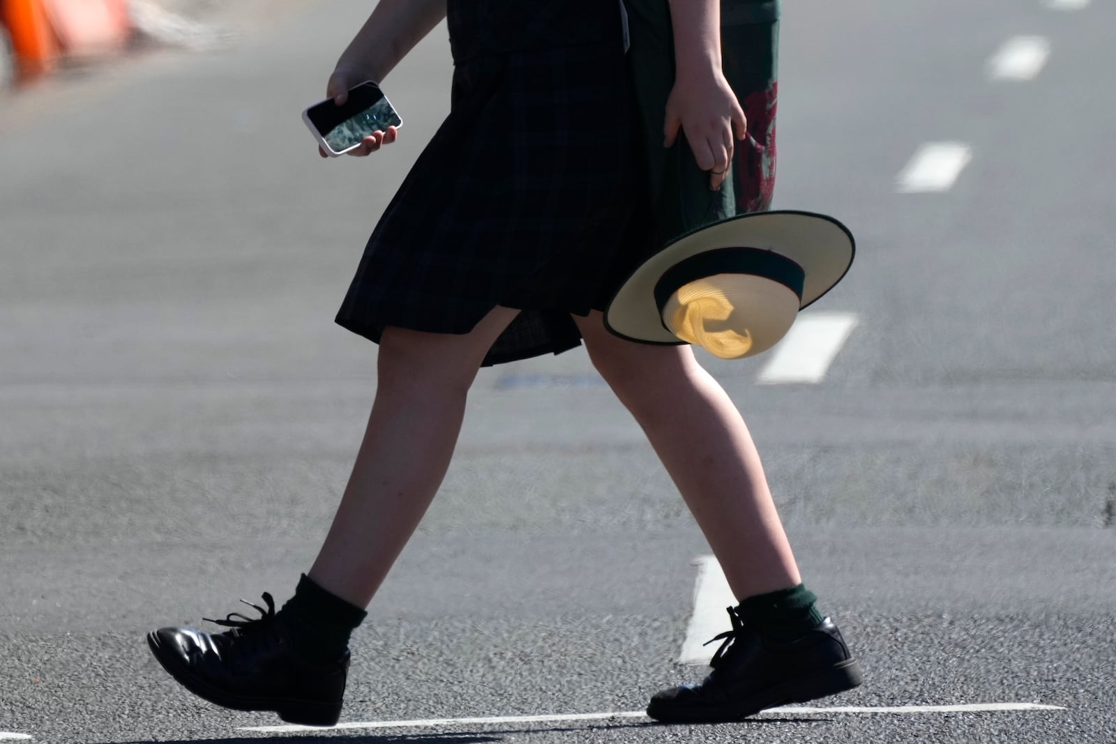 FILE -A school girl holds her phone while crossing a street in Sydney, on Nov. 8, 2024. (AP Photo/Rick Rycroft, File)
