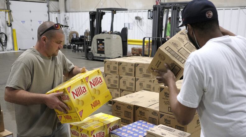 Terry Engle, left, and Kris Munnerlyn, right stack boxes of food while Garrett Wallen operates the fork lift in the warehouse at the Second Harvest Food Bank Thursday. Bill Lackey/Staff