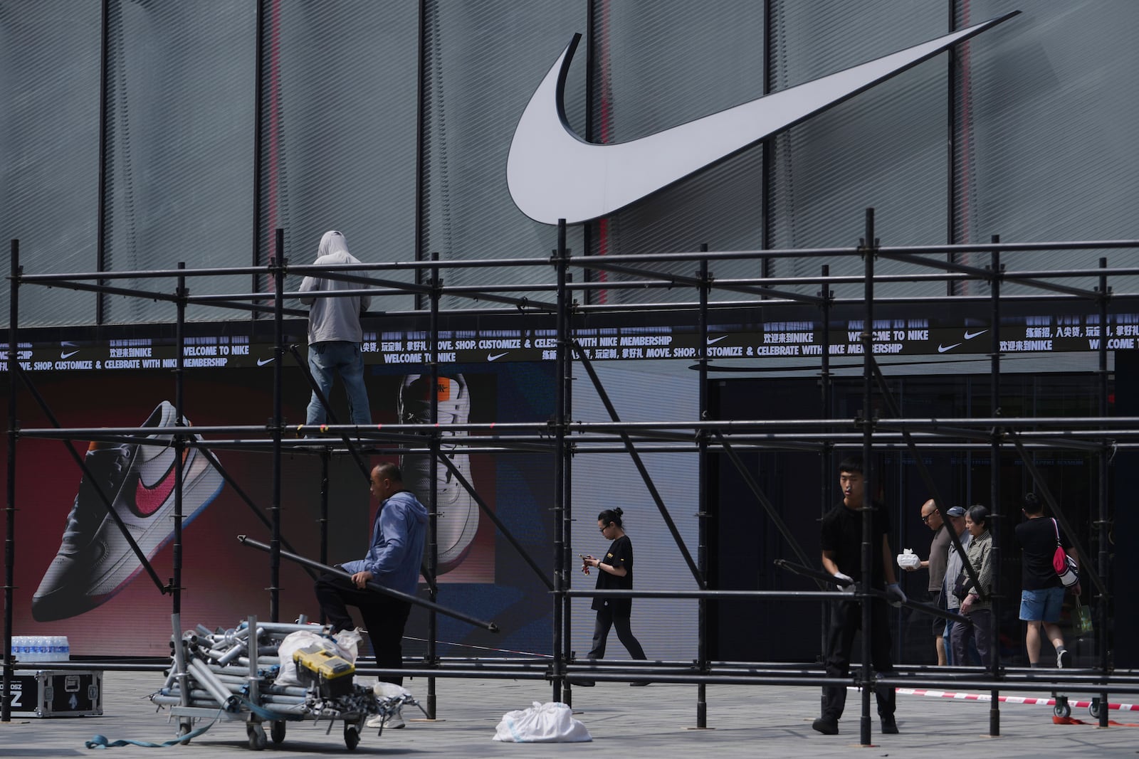 Shoppers walk by as workers install a platform near a Nike store outside a shopping mall in Beijing, Sunday, May 11, 2025. (AP Photo/Andy Wong)