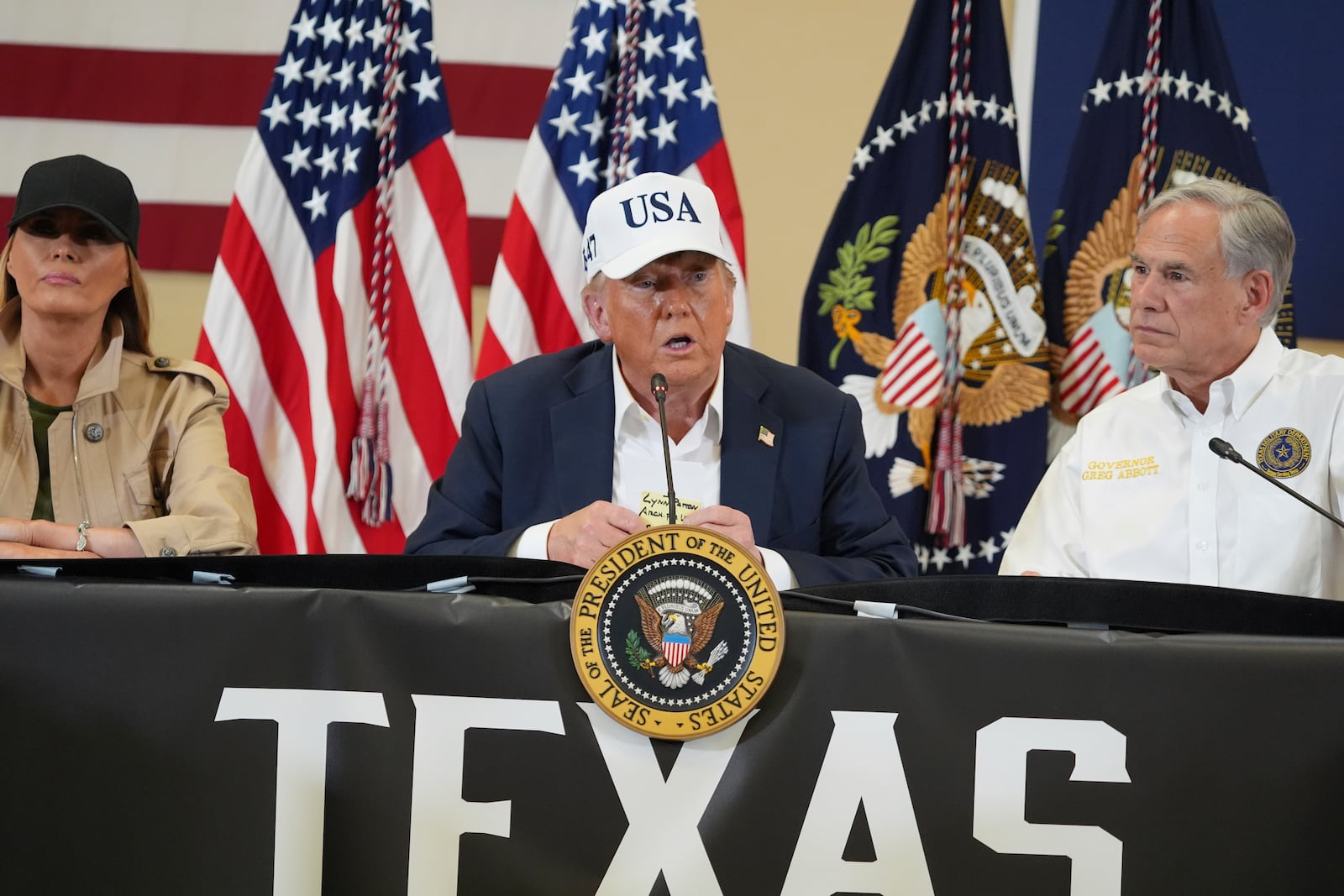 President Donald Trump speaks as first lady Melania Trump, left, and Texas Gov. Greg Abbott listen during a roundtable discussion with first responders and local officials at Hill Country Youth Event Center in Kerrville, Texas, during a tour to observe flood damage, Friday, July 11, 2025. (AP Photo/Jacquelyn Martin)