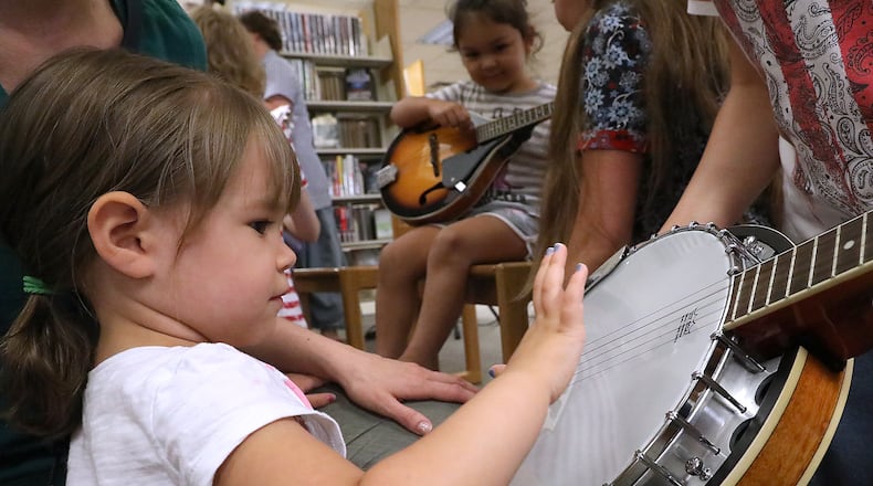 Evie Lombard, 3, plucks the strings of a banjo Monday eveniing at the New Carlisle Library during an instrument petting zoo. Bluegrass music echoed through the stacks at the library as the band Lafferty Pike performed. The band's performance and instrument petting zoo that followed was part of the "Libraries Rock" summer reading program at the library. BILL LACKEY/STAFF
