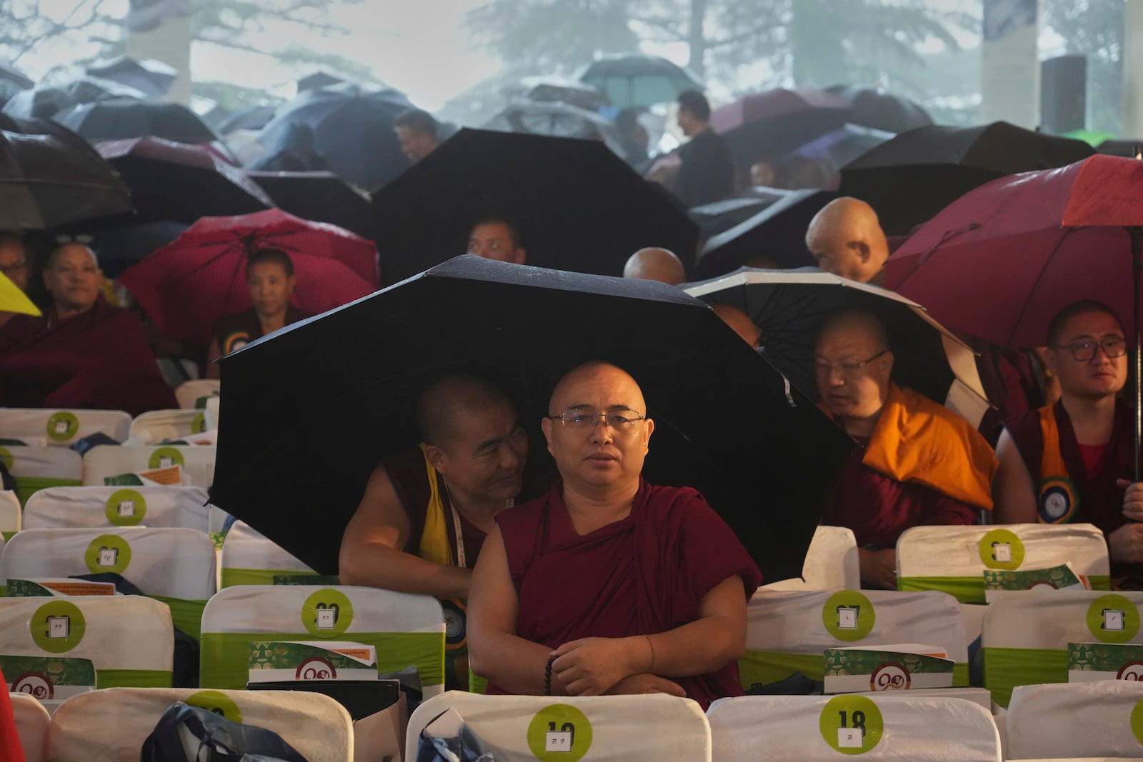 Devotees wait in the rain for the arrival of Tibetan spiritual leader the Dalai Lama to attend an event celebrating his 90th birthday in Dharamshala, India, Sunday, July 6, 2025. (AP Photo/Ashwini Bhatia)