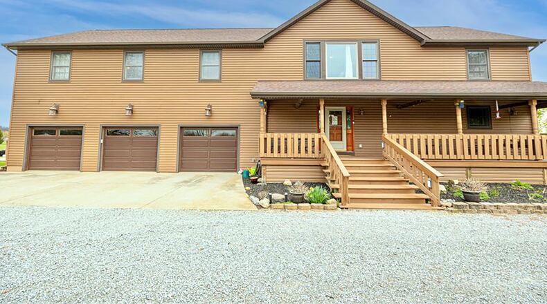 The front of the home features a covered wood front porch with railings and wood beams on the ceiling. The three car attached garage has extended area with a workshop.