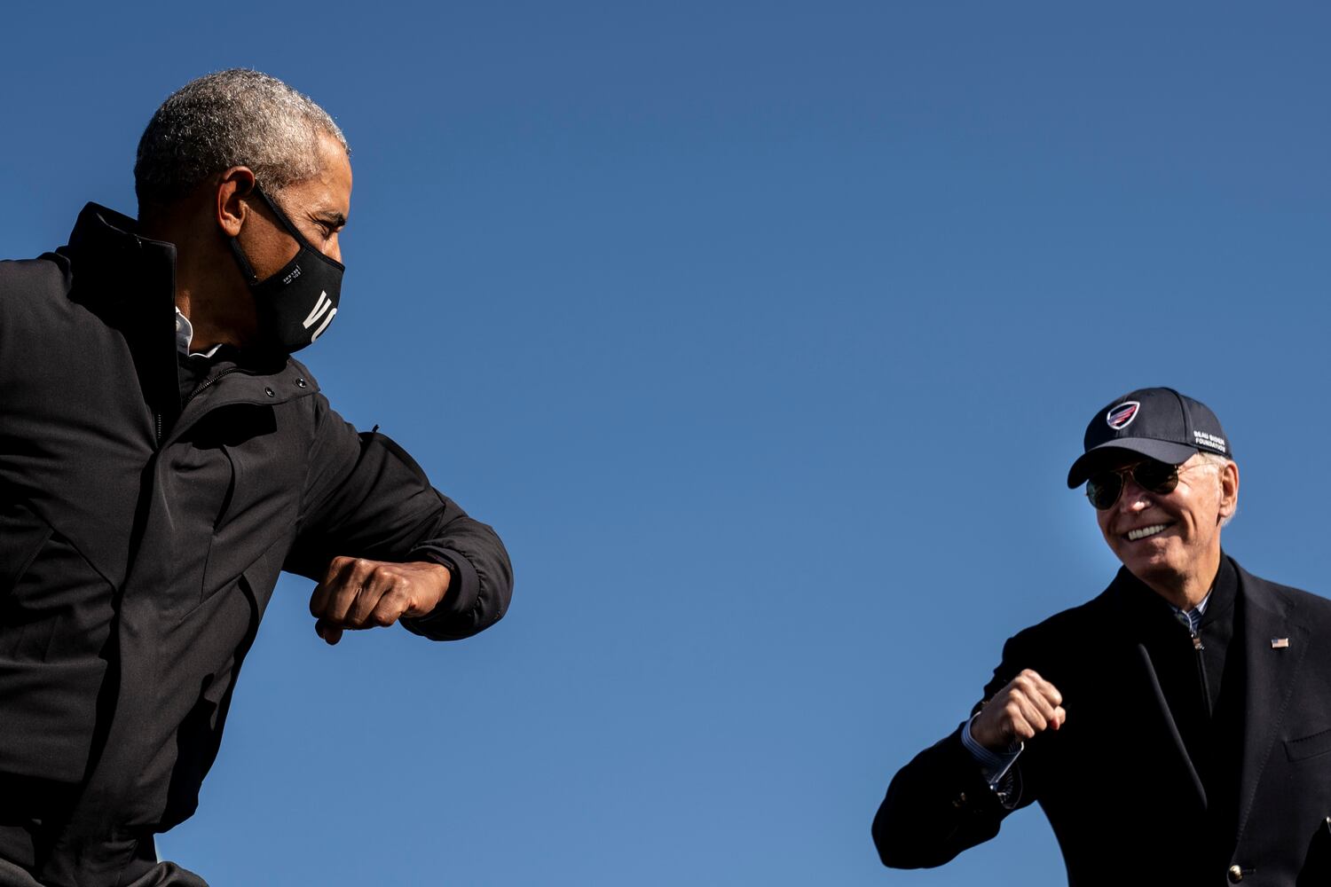 Former President Barack Obama and Joe Biden, the Democratic presidential nominee, gesture to each other at a drive-in campaign rally in Flint, Mich., Oct. 31, 2020. Biden has spent his career devoted to institutions and relationships. And those are the tools he will rely on to govern a fractured nation. (Erin Schaff/The New York Times)
