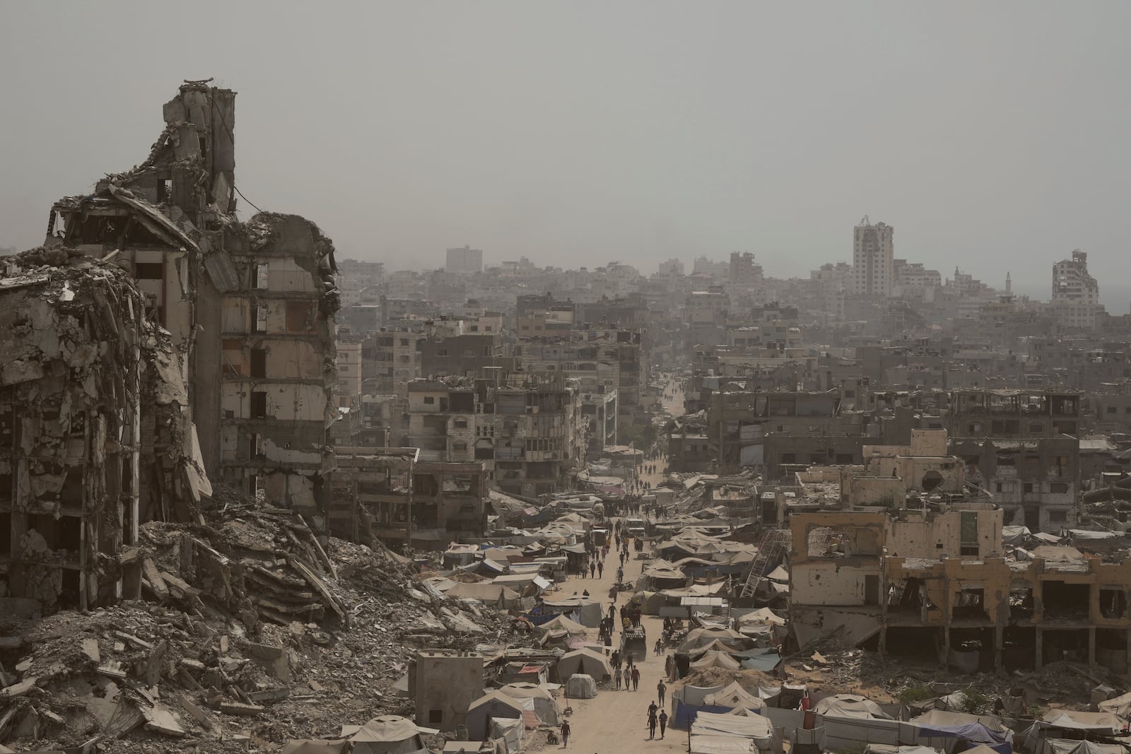 People walk along a street lined with destroyed buildings following Israeli bombardments during the Israel-Hamas war in the Gaza Strip, Tuesday, July 29, 2025. (AP Photo/Jehad Alshrafi)