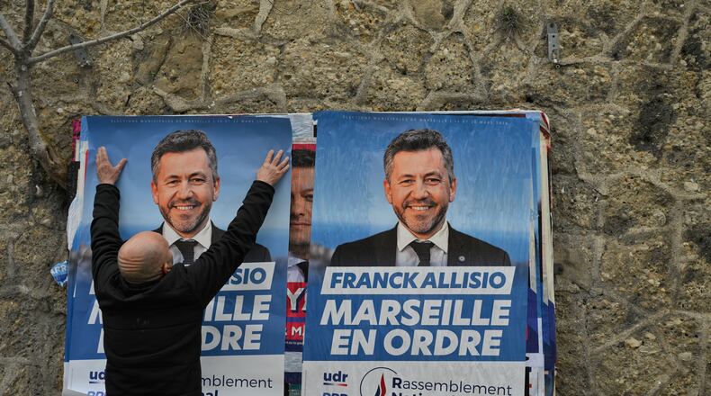 A supporter of far-right candidate Franck Allisio, pastes an electoral poster ahead of the first round of the mayoral elections, in Marseille, south of France, Friday, March 6, 2026. (AP Photo/Philippe Magoni)
