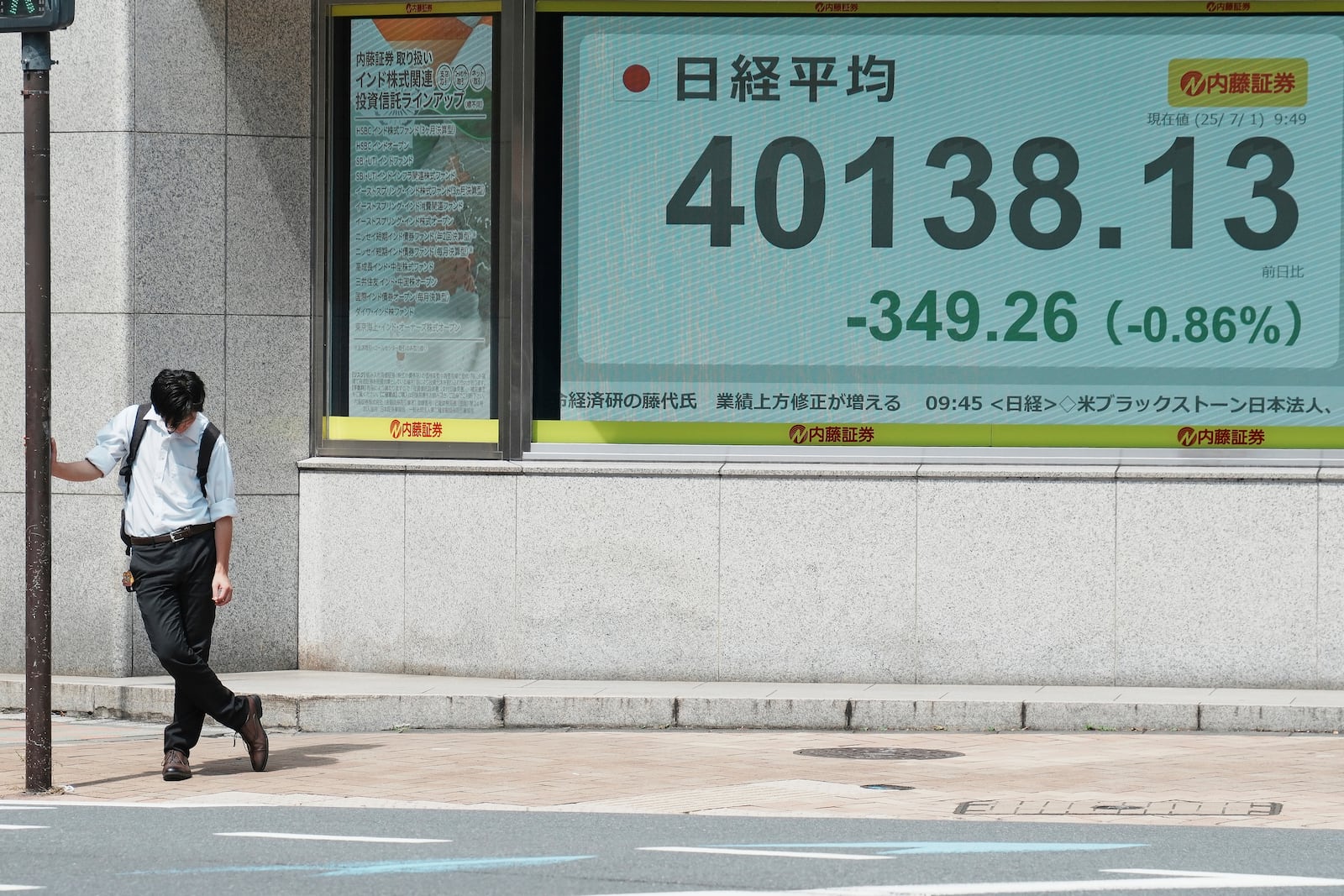A person rests under the intense sun near an electronic stock board displaying Japan's Nikkei index at a securities firm Tuesday, July 1, 2025, in Tokyo. (AP Photo/Eugene Hoshiko)