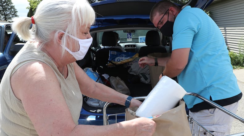 Volunteers Cindy Banks and Marcus Franck load groceries into the back of a car outside outside the Enon Emergency Relief pantry Monday. BILL LACKEY/STAFF