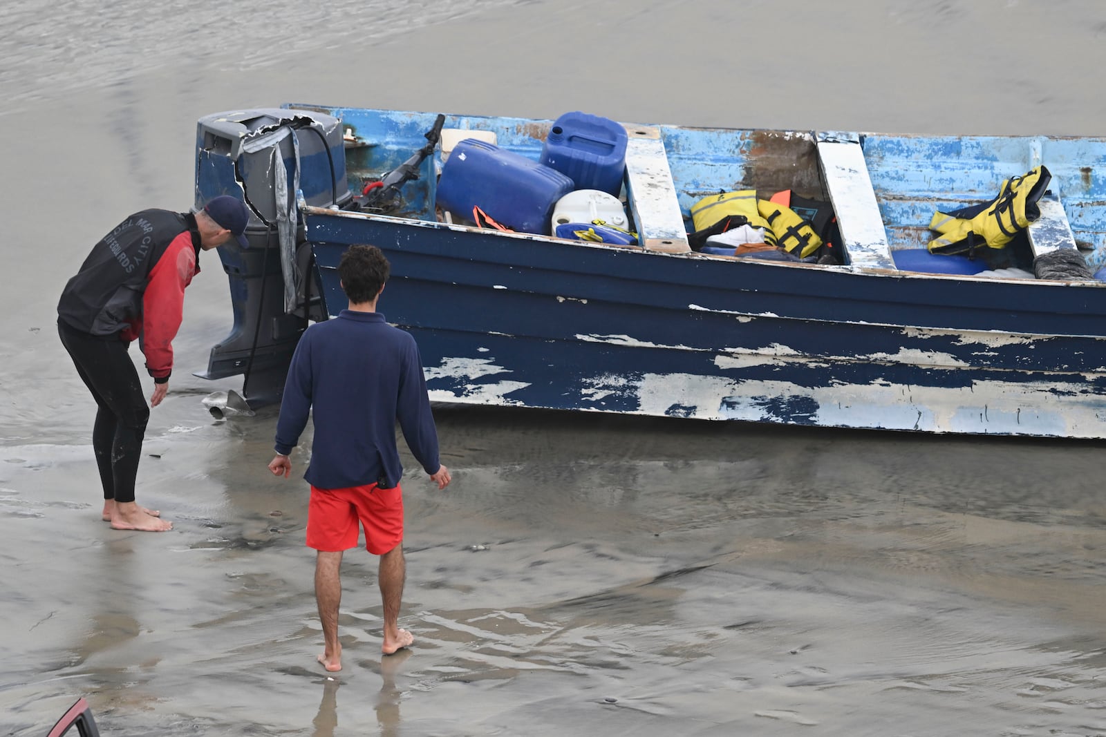 Del Mar lifeguards looks over a capsized boat on the beach Monday, May 5, 2025, in at Torrey Pines State beach in San Diego, Calif. (AP Photo/Denis Poroy)