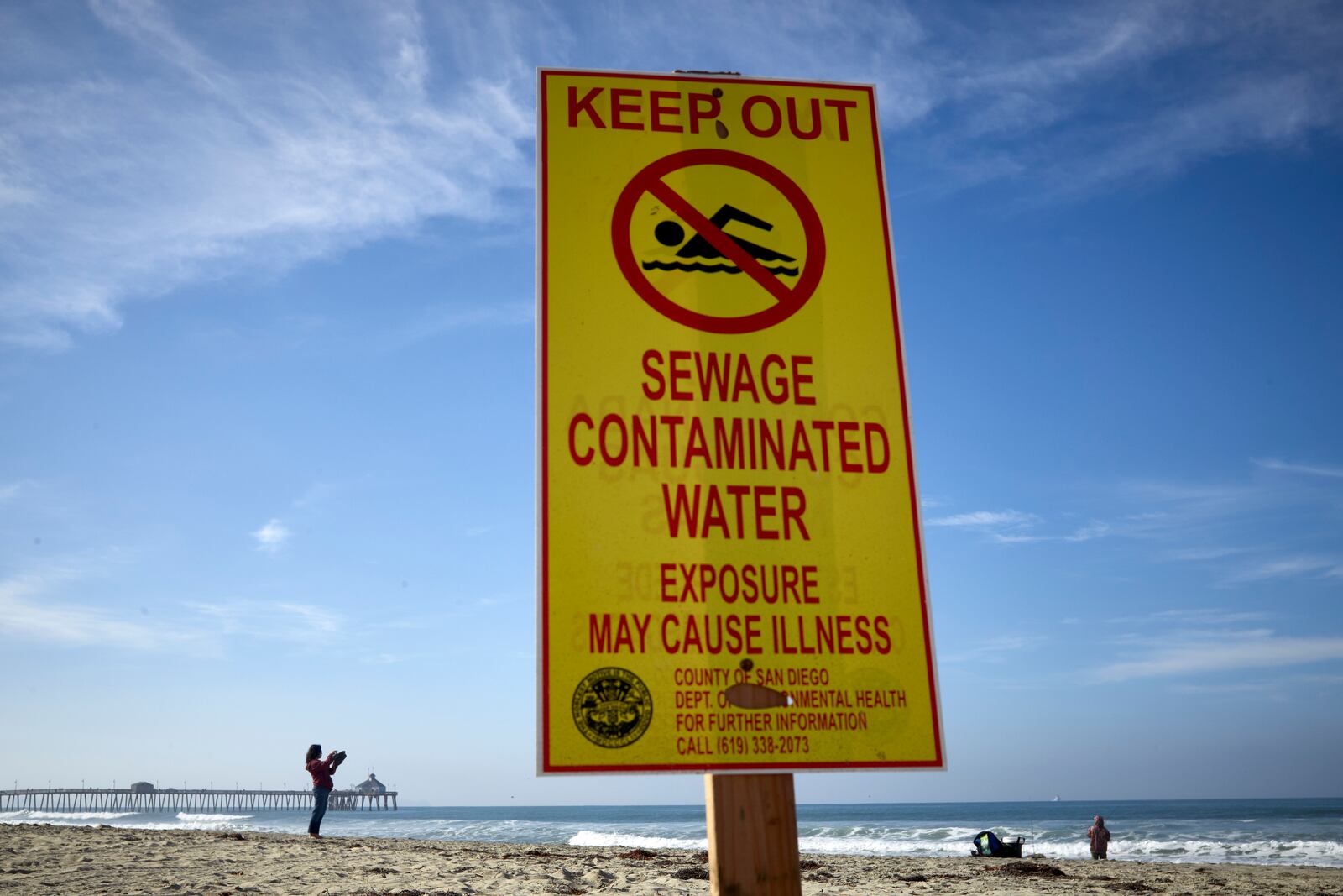 FILE - A woman records with a phone along the beach as a sign warns of contaminated water Dec. 12, 2018, at Imperial Beach, Calif. (AP Photo/Gregory Bull, File)