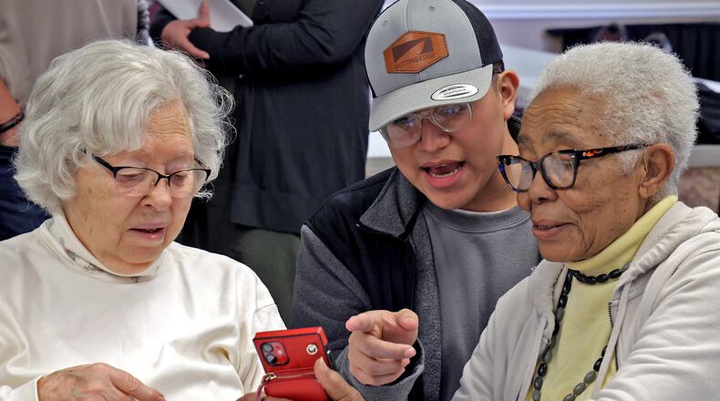 Cristian Portillo, a student at the Springfield/Clark CTC, helps Oakwood Village residents, Mary Chatfield, left, and Beatrice Smith with their cell phones Monday, Feb. 24, 2024. Cristian and several cybersecurity students visited Oakwood Village to talk about how to avoid scams on the internet and answer any questions the residents had about their portable devices. BILL LACKEY/STAFF
