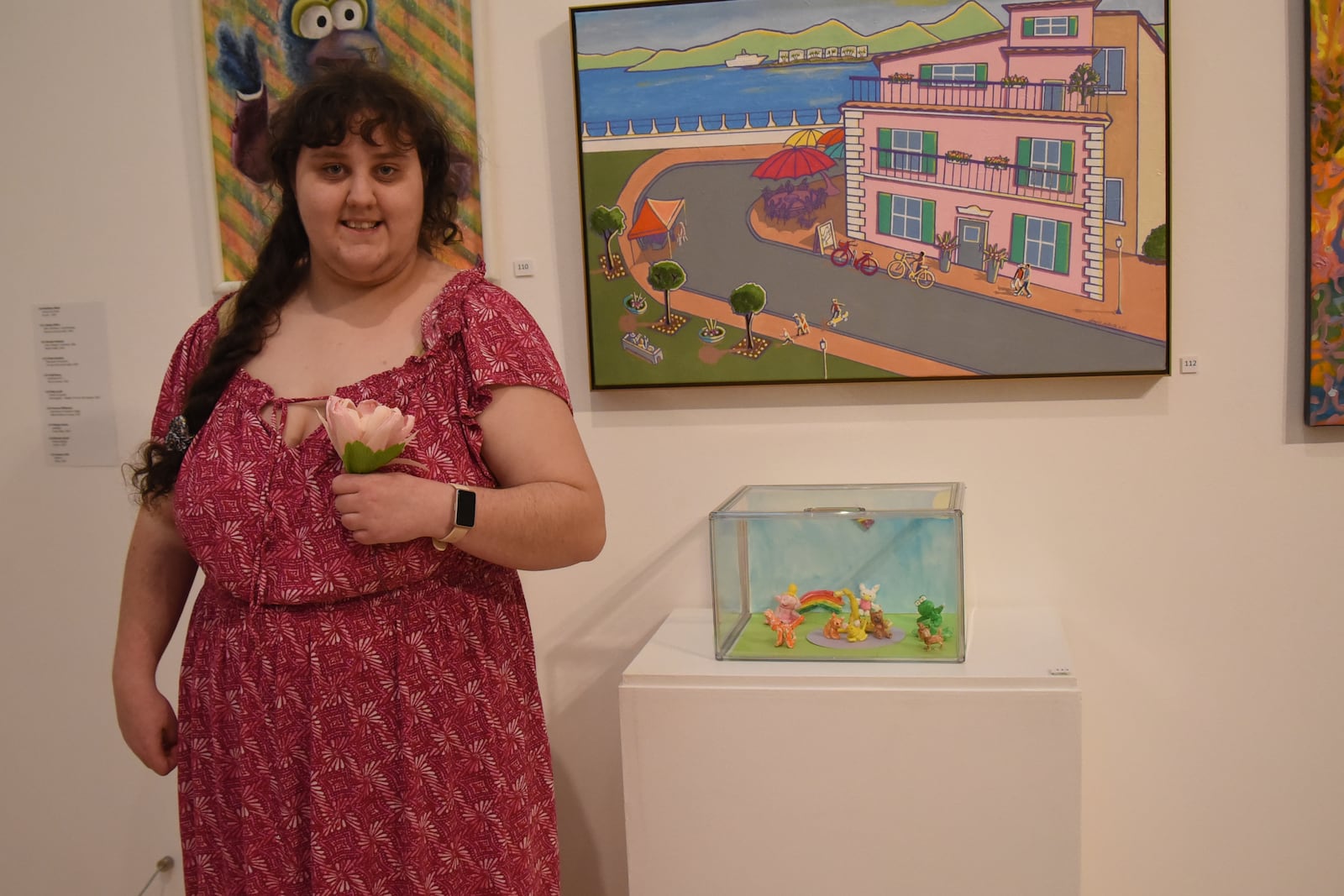 Chloe Gardner holds a flower next to her work, which is in a case to her left, at the Springfield Museum of Art’s McGregor Gallery as part of the museum's 79th Juried Members’ Exhibition during a showcase on Nov. 6, 2025. CONTRIBUTED