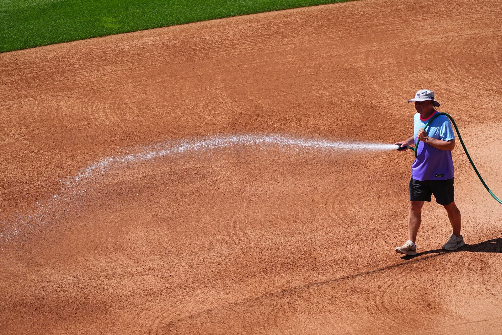 Coors Field head groundskeeper Mark Razum wets down the skin of the infield for a baseball game between the Arizona Diamondbacks and the Colorado Rockies as a heat dome packing triple-digit daytime high temperatures sweeps over the intermountain west Friday, June 20, 2025, in Denver. (AP Photo/David Zalubowski)