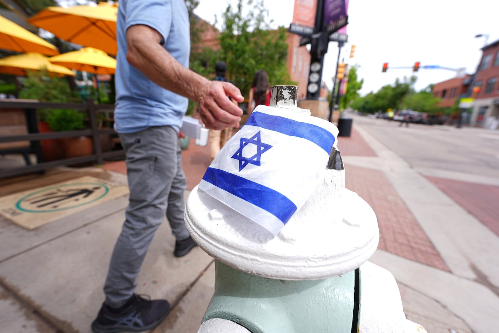A passer-by touches the flag of Israel taped on to the top of a bollard on the east end of the Pearl Street Mall near the Boulder County, Colo., courthouse Monday, June 2, 2025, in Boulder, Colo. (AP Photo/David Zalubowski)