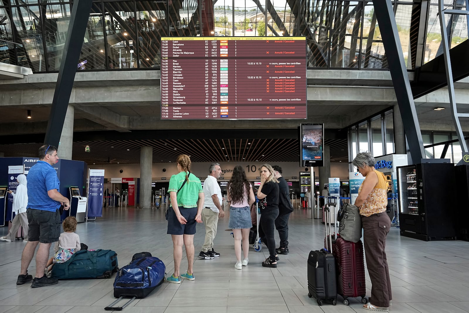 Passengers look a departures information board at Saint-Exupery airport, near Lyon, as French air traffic controllers launched a two-day strike to demand better working conditions, Friday, July 4, 2025. (AP Photo/Laurent Cipriani)
