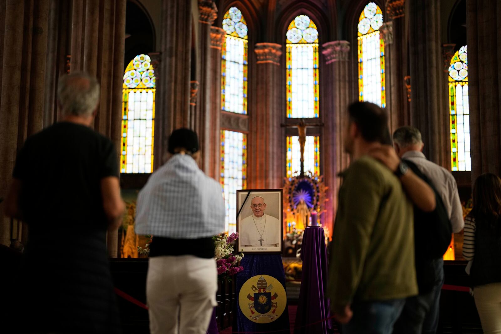People stand next to a photograph of Pope Francis placed at Saint Anthony Catholic church in Istanbul, Turkey, Monday, April 21, 2025. (AP Photo/Khalil Hamra)