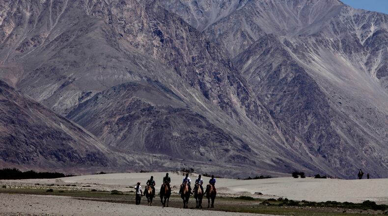 FILE- In this July 20, 2011 file photo, tourists ride double hump camels at Nubra valley, in Ladakh, India. Tensions along the disputed India-China border seem to be getting worse rather than better, three months after their deadliest confrontation in decades in June. The Asian giants accused each other this week of sending soldiers into each other’s territory and fired warning shots for the first time in 45 years, raising the specter of full-scale military conflict. (AP Photo/Channi Anand, File)