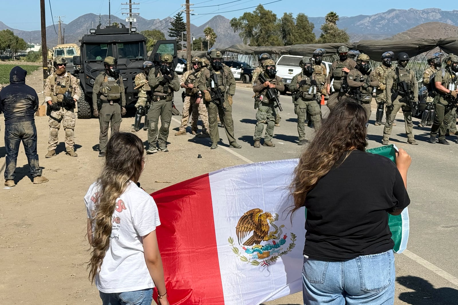 Demonstrators hold a flag in front of federal agents blocking a road during an immigration raid in Camarillo, Calif. (AP Photo/Michael Owen Baker)