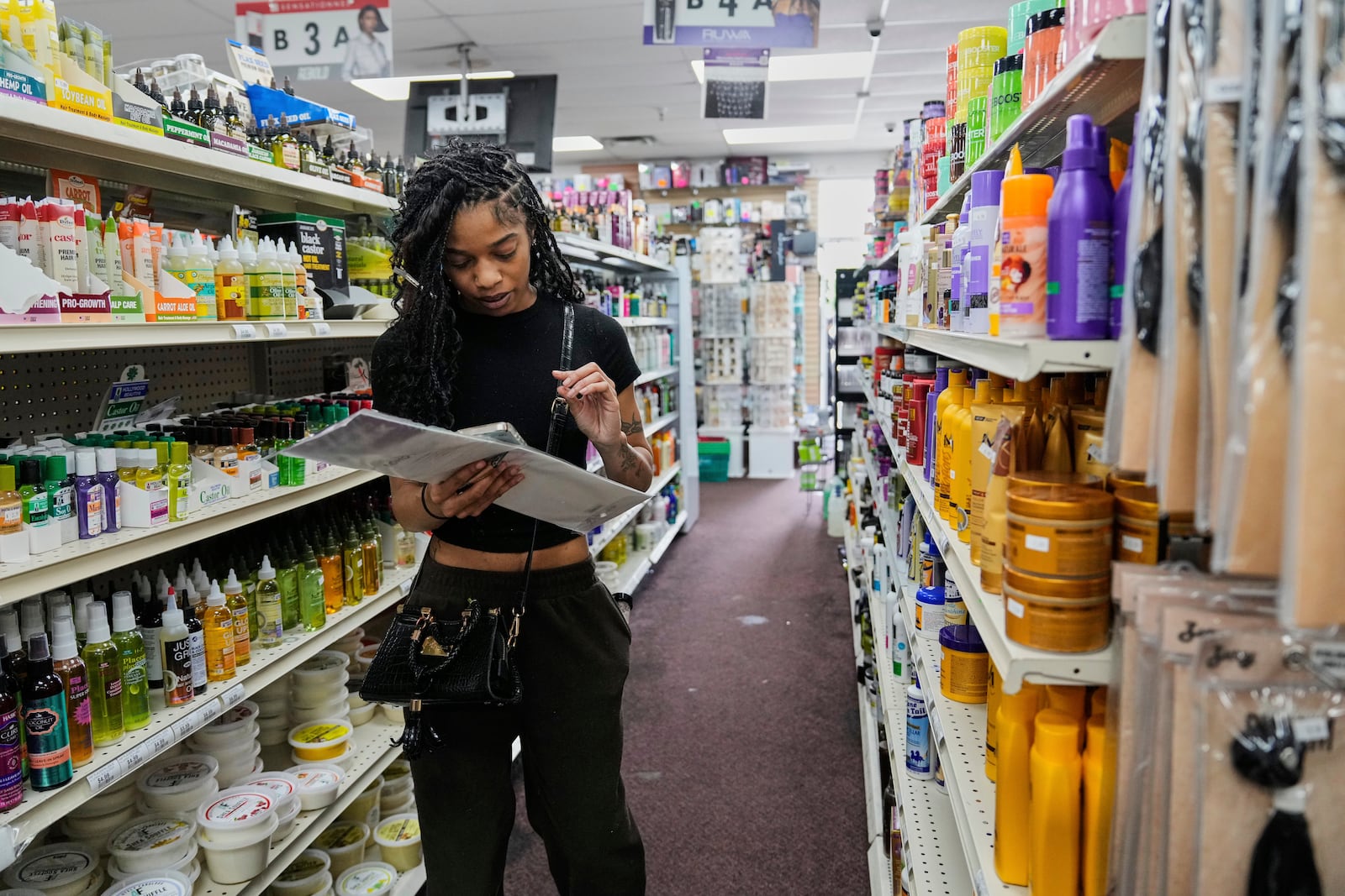 Leilani Martin checks a list on her phone while shopping for supplies that she ran out of while braiding her hair, Tuesday, May 6, 2025, at Essence Beauty, a beauty supply store in Union City, Ga. (AP Photo/Stephanie Scarbrough)