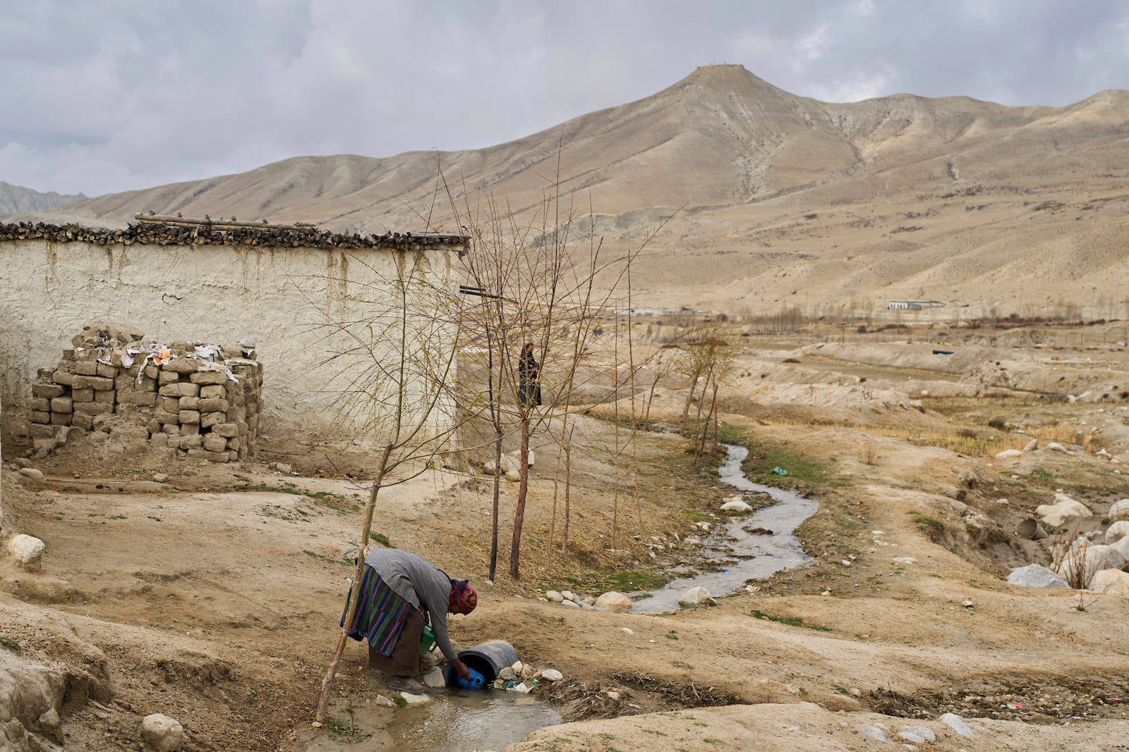 A woman collects water at the newly relocated settlement of the abandoned Samjung village in the Mustang region, 462 kilometers (288 miles) west of Kathmandu, Nepal, Saturday, April 19, 2025. (AP Photo/Niranjan Shrestha)