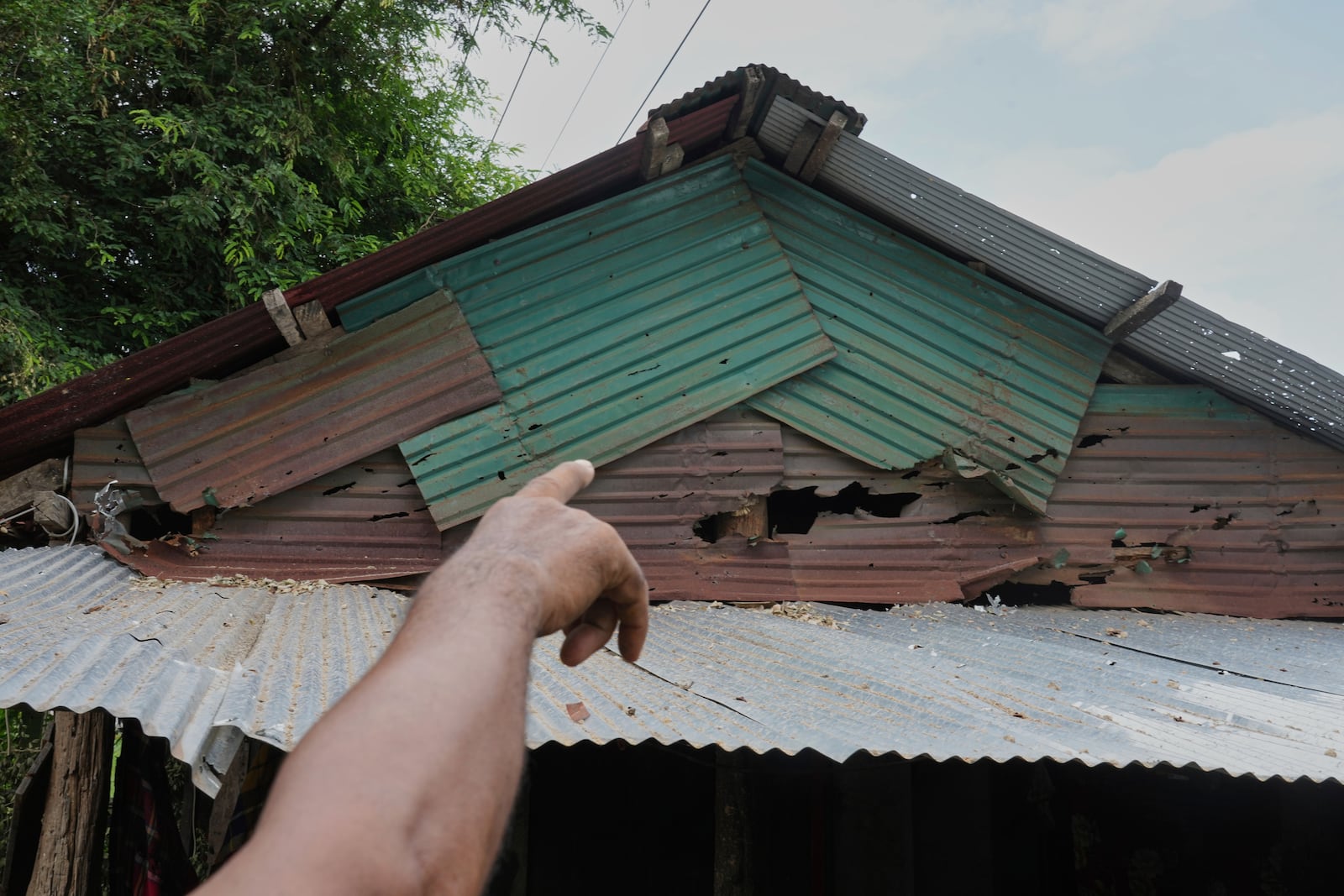 A Cambodian villager points to the roof of a house damaged apparently due to firing from Thailand side in Phrong village, Oddar Meanchey province, Cambodia, Wednesday, July 30, 2025. (AP Photo/Heng Sinith)