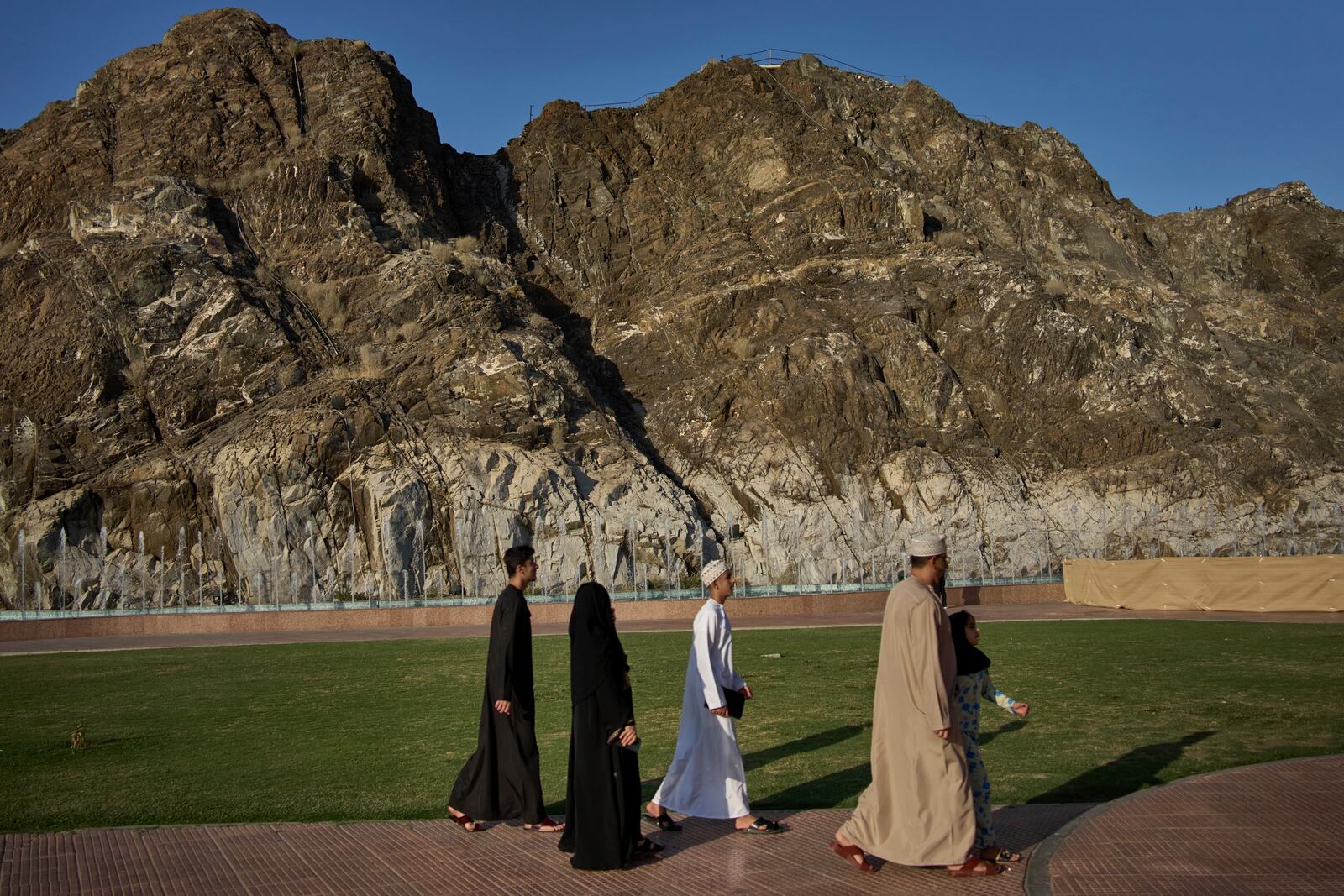 A group of Omani individuals walks in formation along a pathway framed by the rugged cliffs of Muscat, Oman, Friday, April 11, 2025. (AP Photo/ Fatima Shbair)