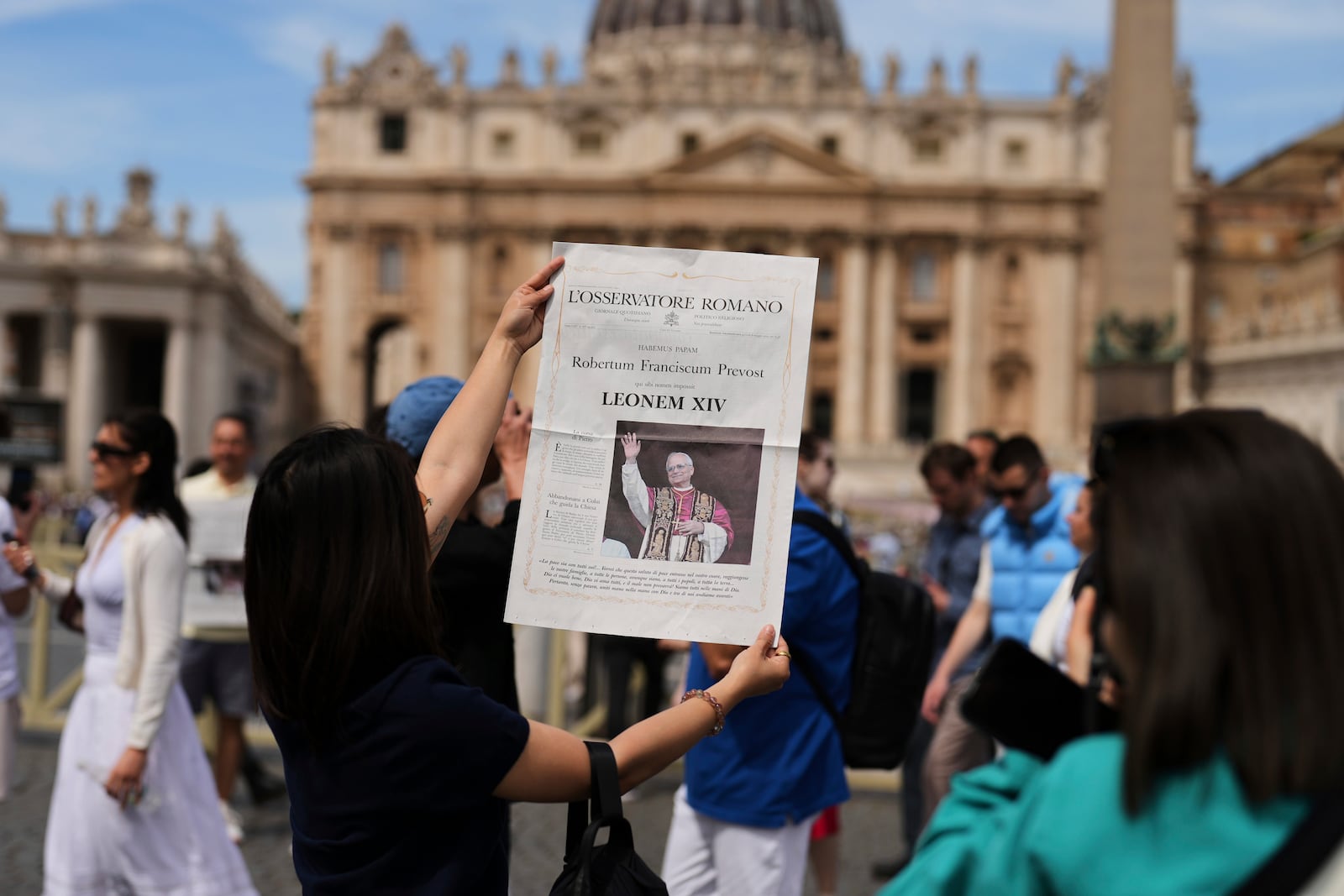 Tourists take photographs with a L'Osservatore Romano newspaper with the image of Pope Leo XIV at the Vatican, Friday, May 9, 2025, a day after he was elected history's first North American pope. (AP Photo/Francisco Seco)
