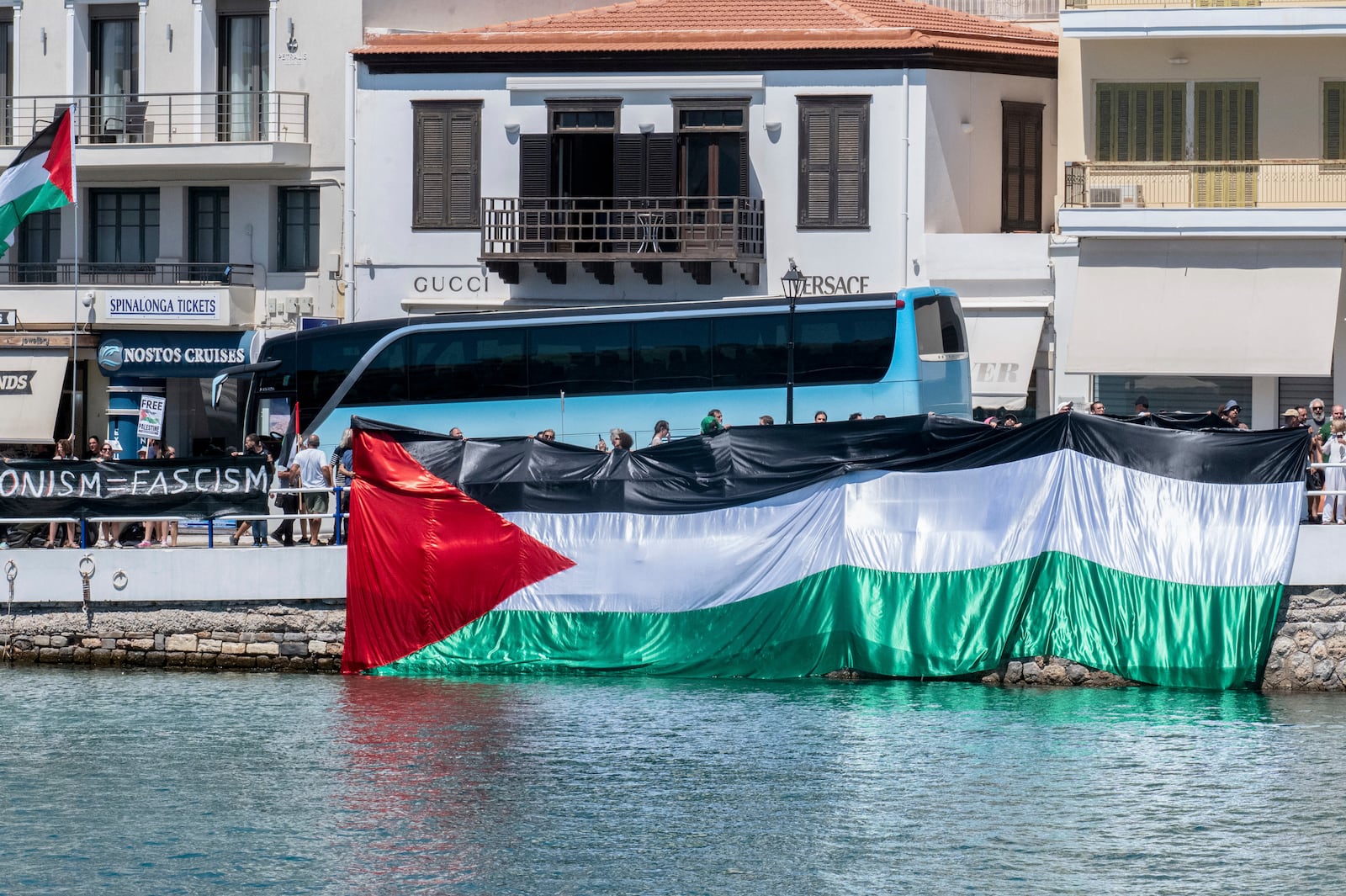 Pro-Palestinians protesters gather during the departure of a ship carrying Israeli tourists, background, in Agios Nikolaos port, on the island of Crete, Greece, Tuesday, July 29, 2025. (Antonis Zouridakis/Eurokinissi via AP)