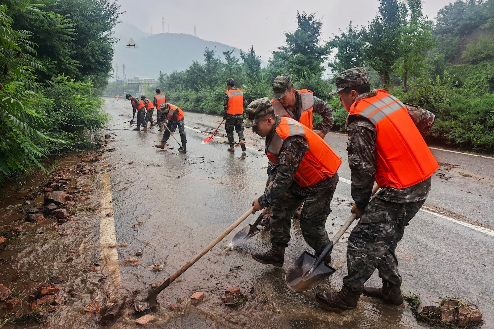 In this photo released by Xinhua News Agency, members of the Chinese People's Armed Police Force clean up silt on a road in Miyun District as continuous rain fall triggers alerts, in north of Beijing on July 27, 2025. (Wang Xiqing/Xinhua via AP)