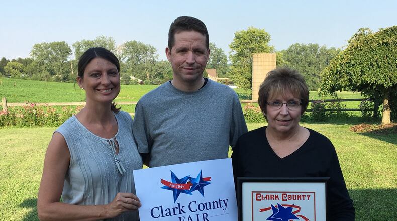 When Marin Smith, left, found out the Clark County Fair was going to update the logo designed by her mother-in-law, Rose, right, who is holding it, she couldn’t think of a better person to do it than her own husband and Rose’s son Jarid, center, shown holding the updated version. Photo courtesy of Marin Smith