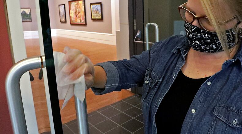 Elizabeth Wetterstroem wipes down door handles on the entry to the galleries at the Springfield Museum of Art in preparation of reopening in July. The museum closed again as coronavirus cases increased. The museum has reopened with new safety precautions. BILL LACKEY/STAFF