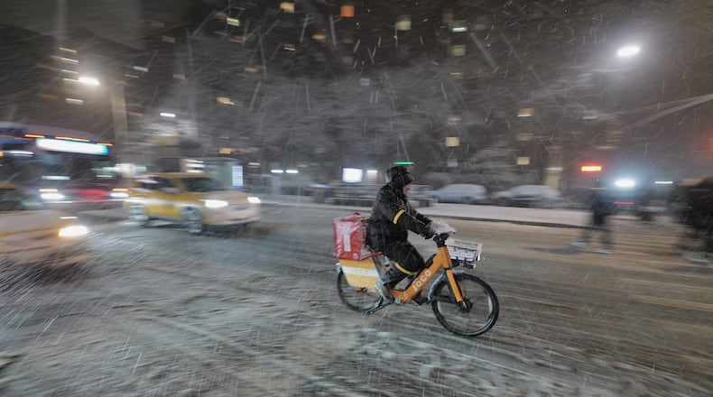 A delivery cyclist travels along 14th Street as snow falls in the Alphabet City neighborhood of New York, Sunday evening, Feb. 22, 2026. (AP Photo/Patrick Sison)