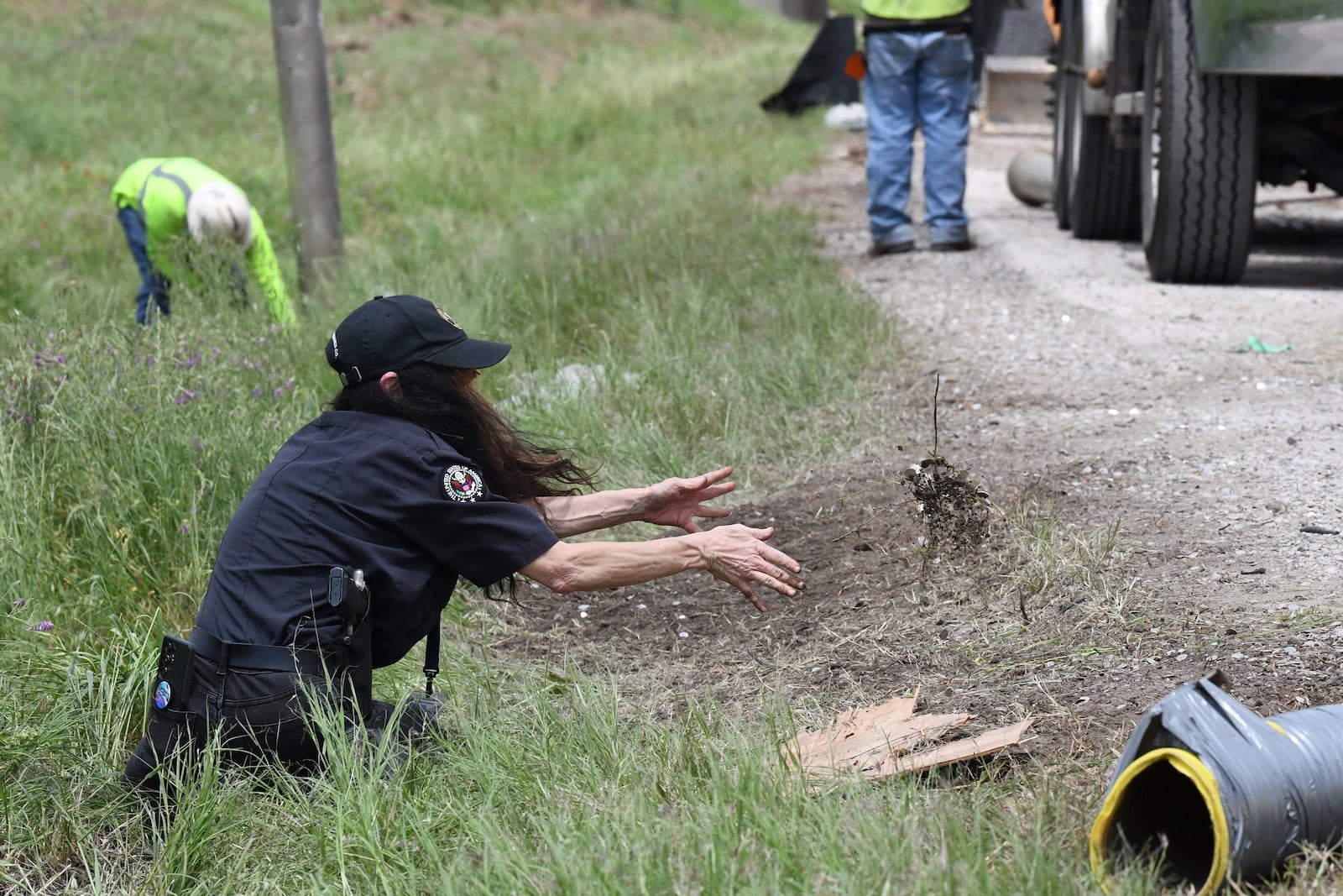 This image provided by the Wise County Messenger shows a United States Armored Co. employee tossing a clump of dirt saturated in dimes along U.S. 81/287 after a rollover caused a currency spill near Alvord High School, Tuesday, April 29, 2025 in Alvord, Texas. (Austin Jackson/Wise County Messenger via AP)