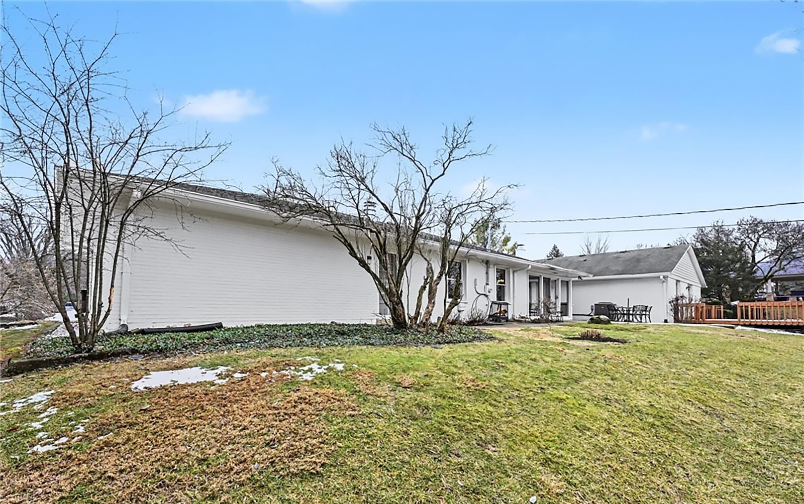 The back of the home features a wood deck with railings and a concrete patio with a walkway. It overlooks mature trees and wood beyond. CONTRIBUTED