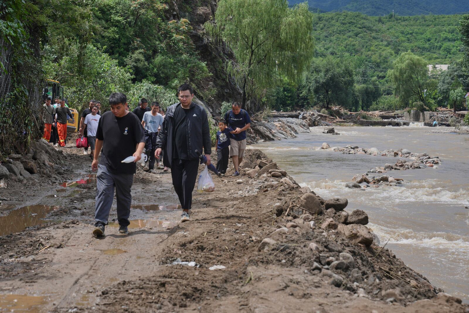 People walk on a road heading to Langjiayu village damaged by flood as they evacuate from the village after heavy rains in Miyun district on the outskirts of Beijing, Tuesday, July 29, 2025. (AP Photo/Andy Wong)