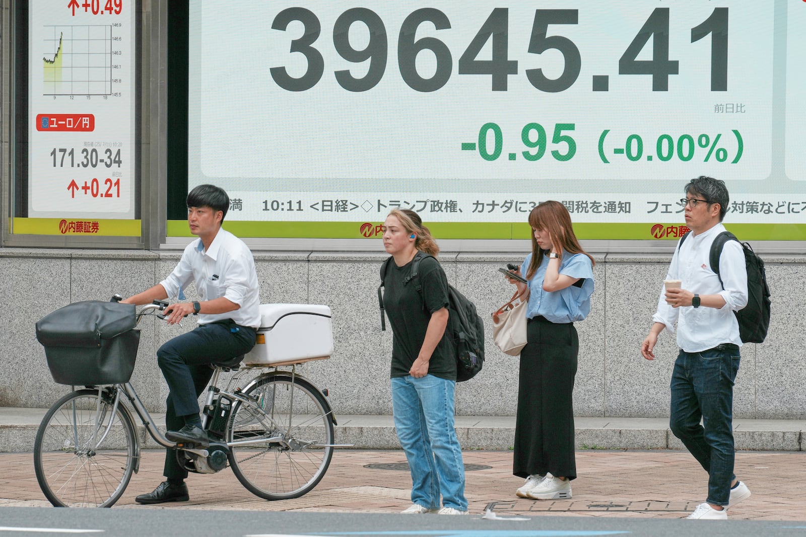 People stand in front of an electronic stock board showing Japan's Nikkei index at a securities firm Friday, July 11, 2025, in Tokyo. (AP Photo/Eugene Hoshiko)