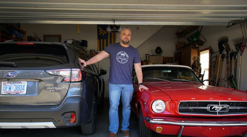 Steve Bock stands between his new Subaru Outback and his 1965 Ford Mustang at his home in Apex, N.C., on Friday, March 5, 2021. He would like to have an electric car, but says the prices will have to come down a lot before he can do it. Opinion polls show that most Americans would consider an EV if it cost less, if more charging stations existed and if a wider variety of models were available. (AP Photo/Allen G. Breed)