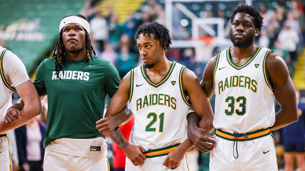 Wright State junior guard Logan Woods (center) links arms with sophomore wing Andrea Holden (left) and graduate forward Michael Imariagbe (right) during the national anthem before an 86-37 win over Franklin College 86-37 in a season opener on Monday, Nov. 3 at Ervin J. Nutter Center in Fairborn. BRYANT BILLING/STAFF
